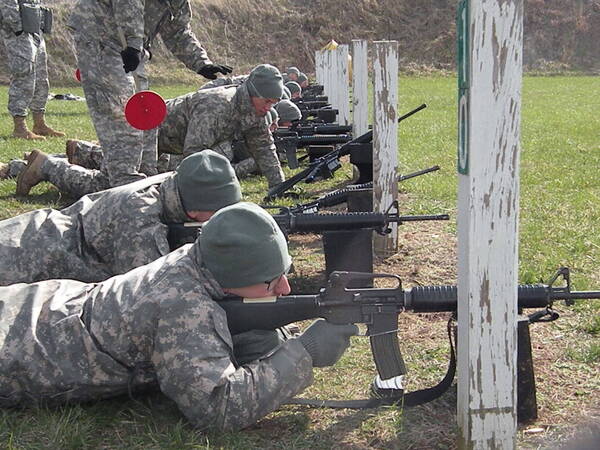 Line of cadets on the ground who are aiming guns at targets on practice shooting range