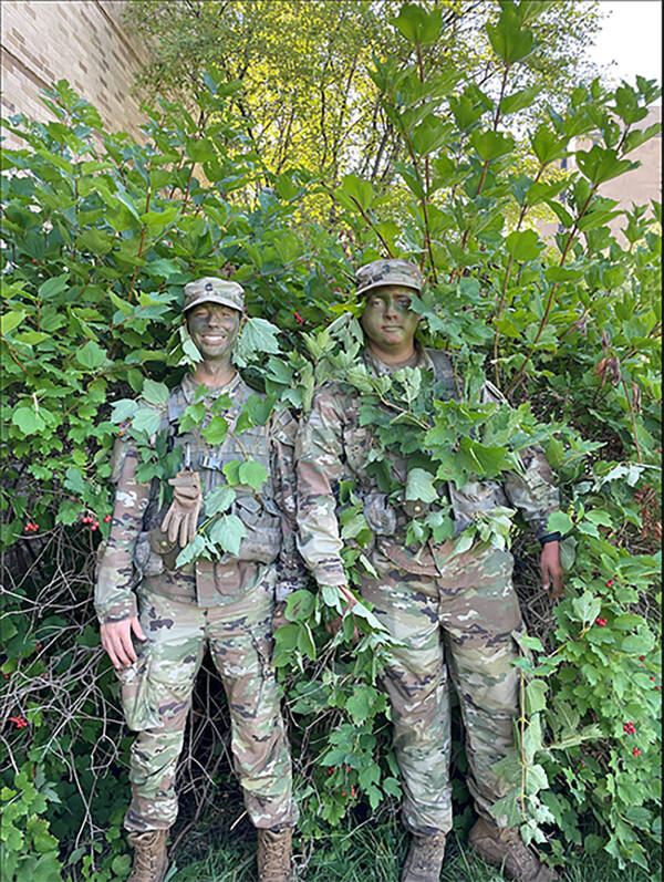 Two cadets with camouflage paint standing in bushes as they work perfect their camouflage skills during our fieldcraft lab