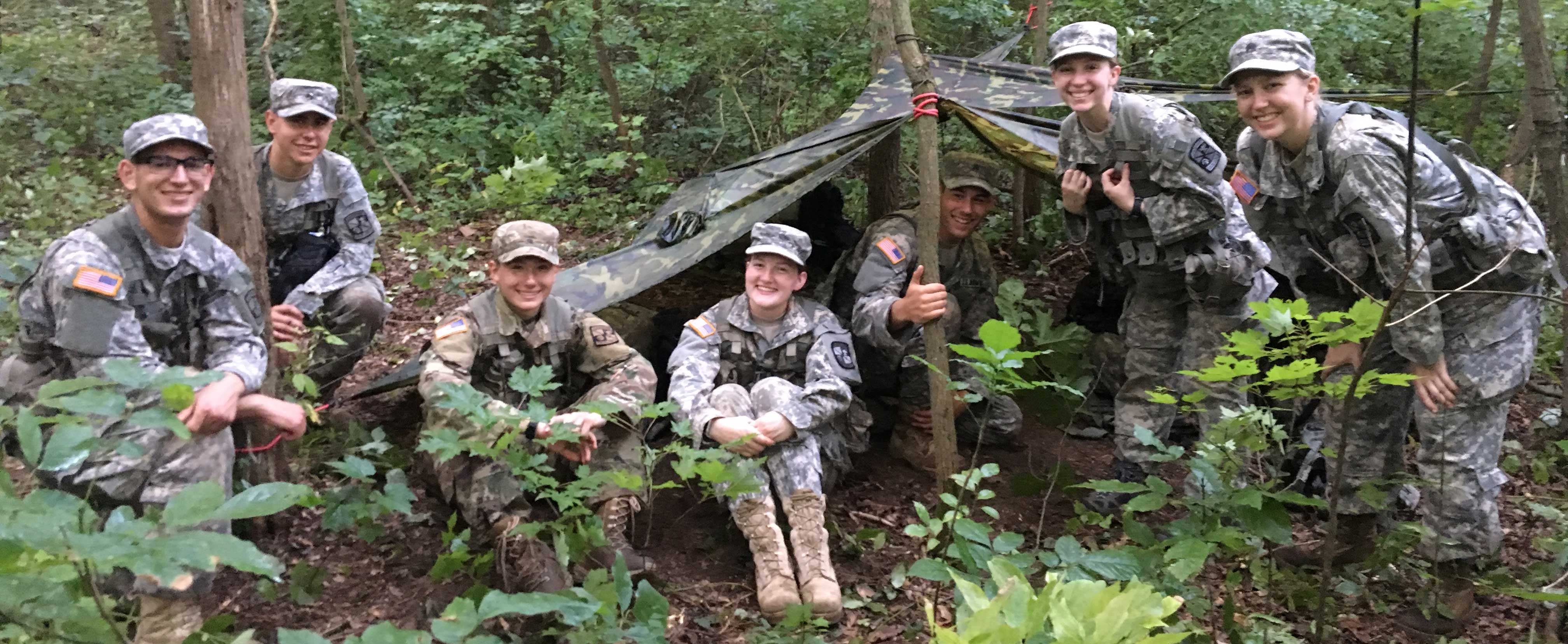 Group of cadets smiling together after setting up a tent in the woods during New Cadet Orientation