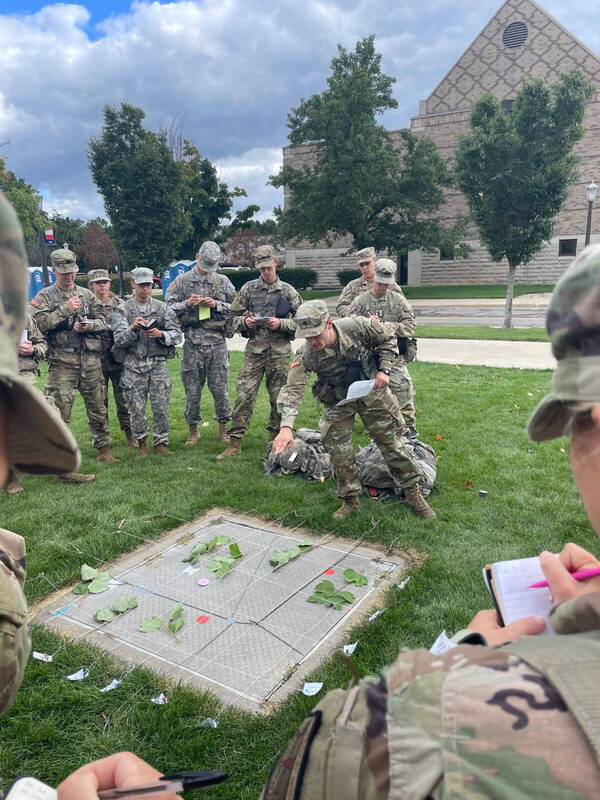 Cadet briefs an operations order using his terrain model kit to a small group of cadets standing around him