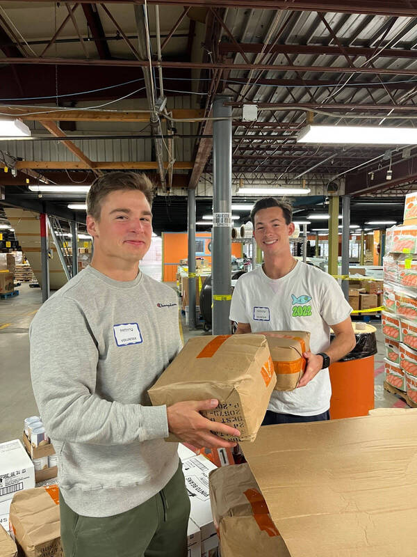 Two young men carrying packages of food in a warehouse setting