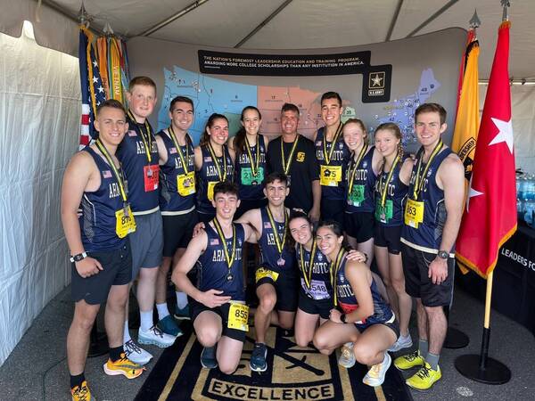 A group of runners wearing uniform and medals pose together in tent after their race