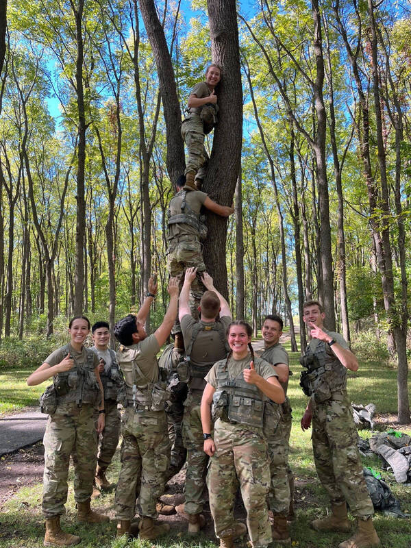 A group of cadets build a human tower to hoist one of the members into a tree