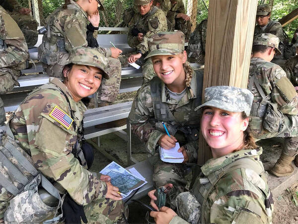 Three female cadets smiling together as they prepare for the Land Navigation exercise. 