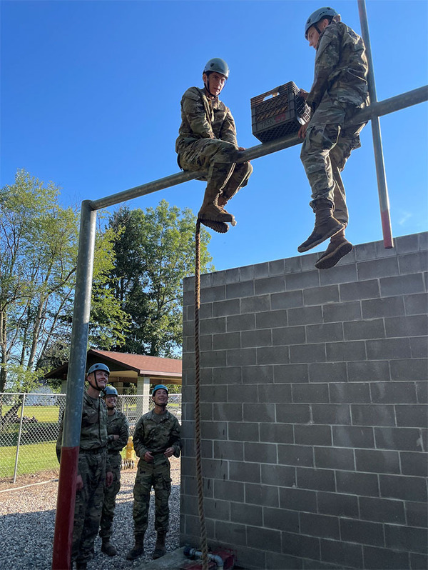Three cadets working together to scale wall, and solve obstacles during the Leader’s Reaction Course.