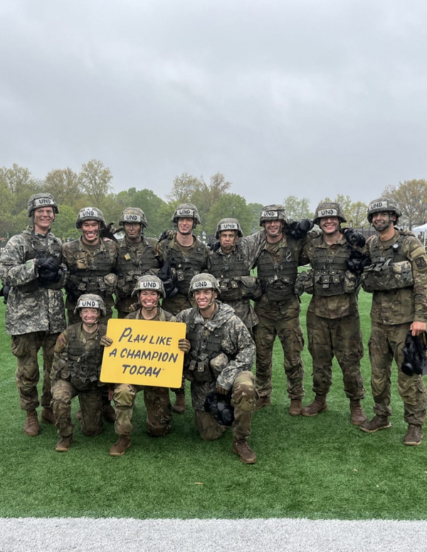 Small group of army cadets dressed in uniform stand around yellow sports sign
