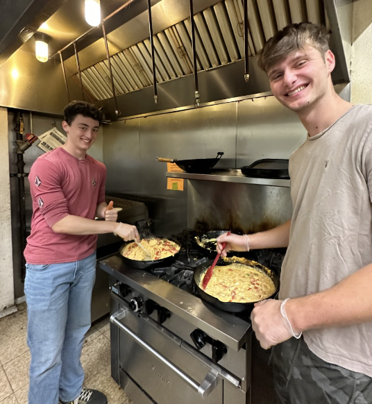 Two young men stirring soup over stove